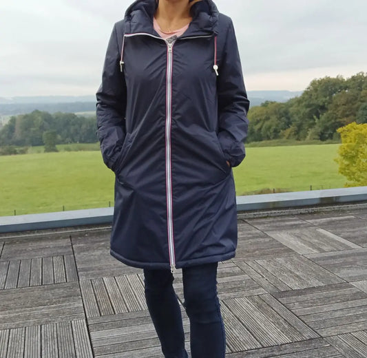 Imperméable long bleu marine pour femme avec capuche et fausse fourrure intérieure, fermeture zippée centrale et poches, taillée jusqu’aux genoux. Laura Jo.