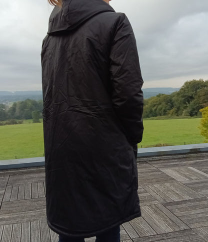 Person wearing long black Laura Jo waterproof coat on wooden deck, outdoor green field view