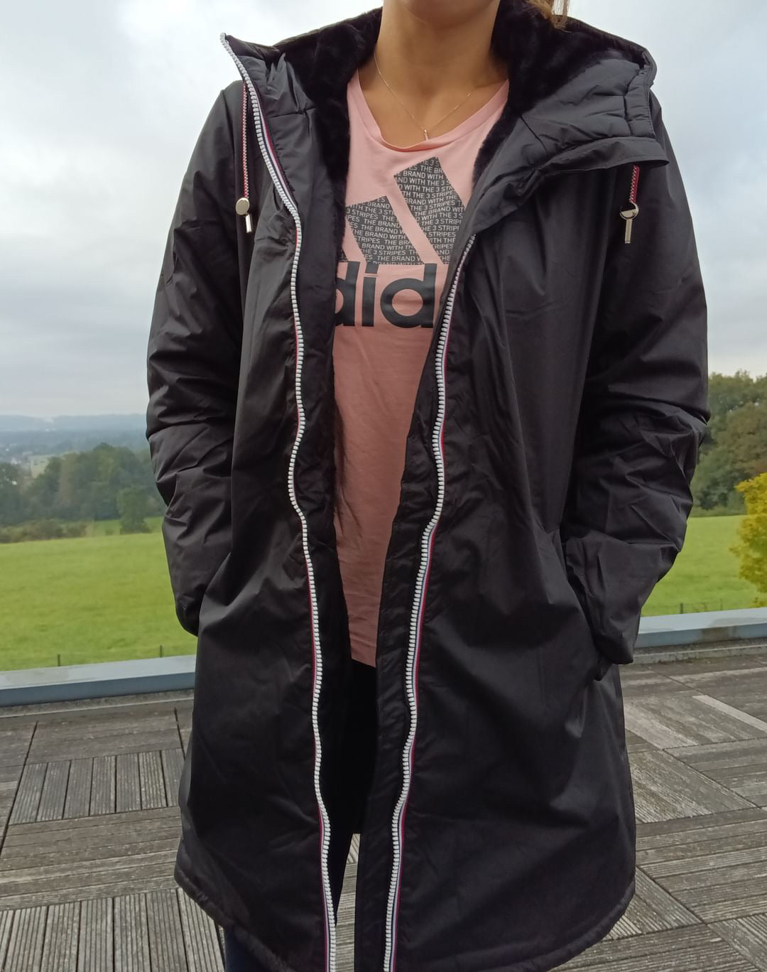 Woman wearing black Laura Jo long waterproof coat with faux fur trim and tricolor drawstring outdoors
