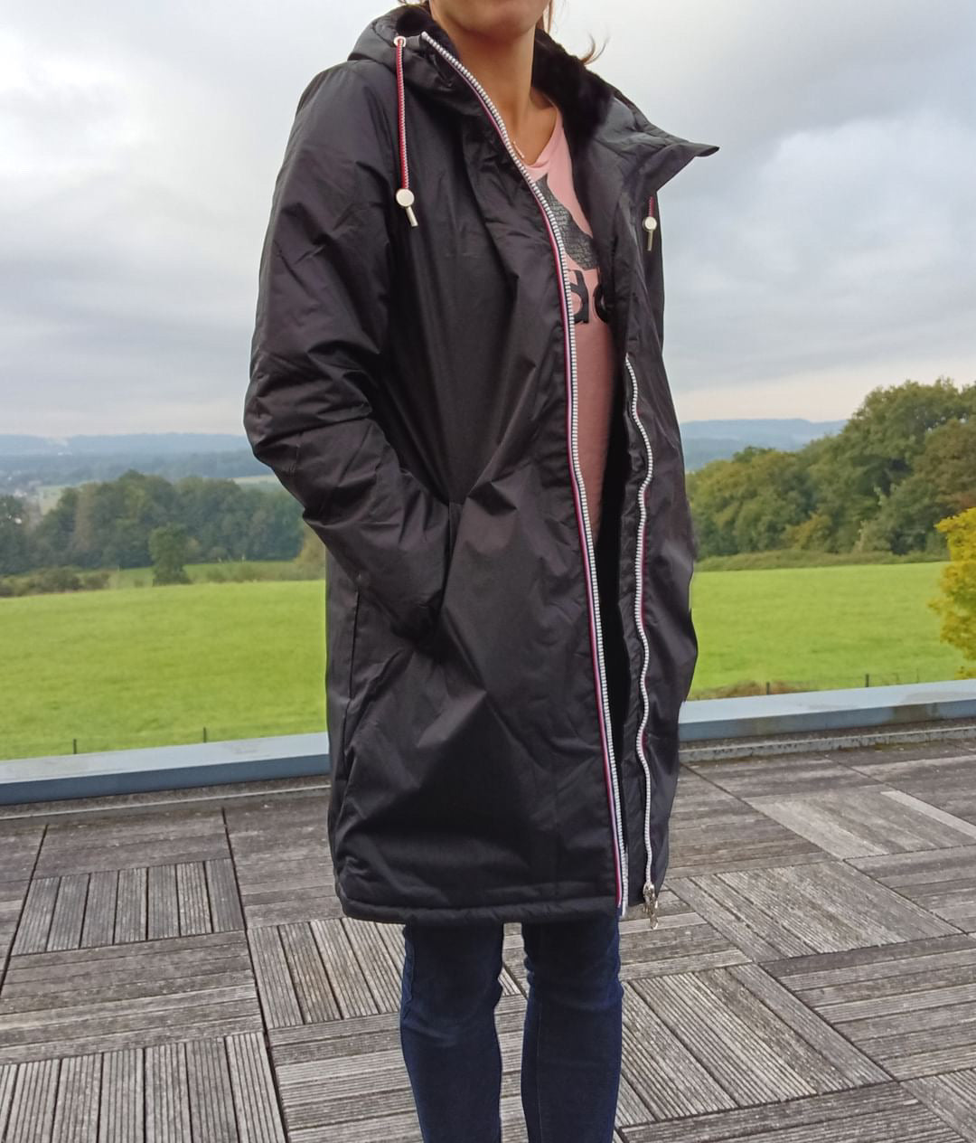 Woman wearing Laura Jo black waterproof long coat with faux fur hood, outdoor setting, Le Petit Placard