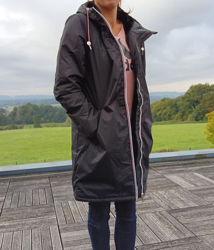 Woman wearing Laura Jo black waterproof long coat with faux fur hood, outdoor setting, Le Petit Placard