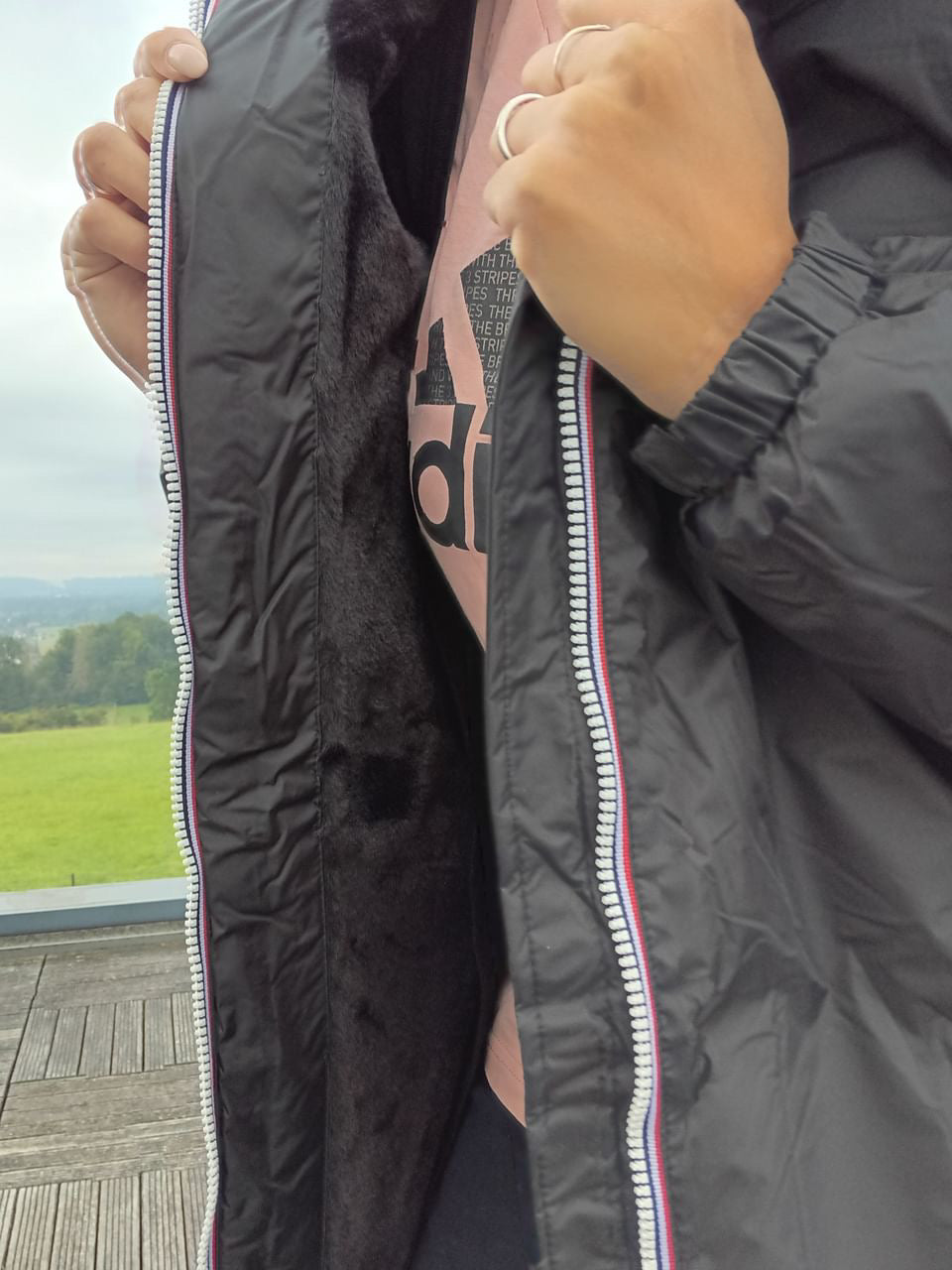 Black Laura Jo raincoat with faux fur lining and tricolor zip, shown open outdoors