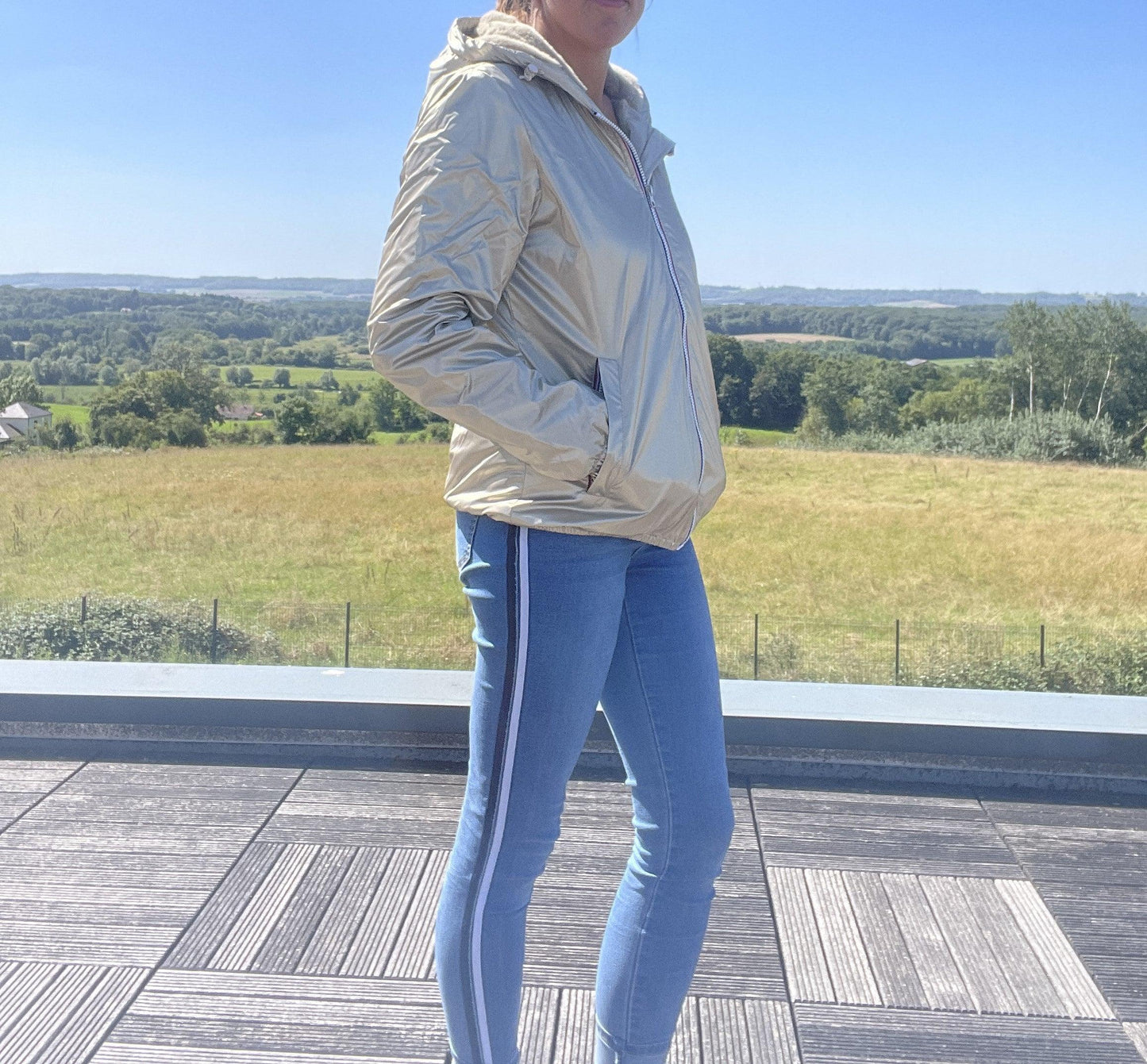 Woman wearing Laura Jo short gold waterproof jacket and jeans outdoors, Le Petit Placard