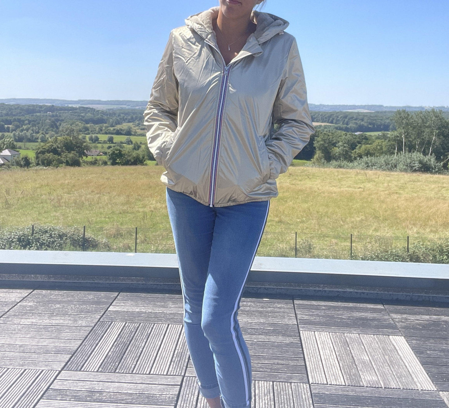 Woman wearing gold Laura Jo short waterproof jacket and blue jeans outdoors at Le Petit Placard