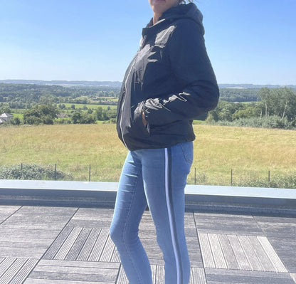 Woman wearing black Laura Jo raincoat and blue jeans on a terrace with scenic countryside