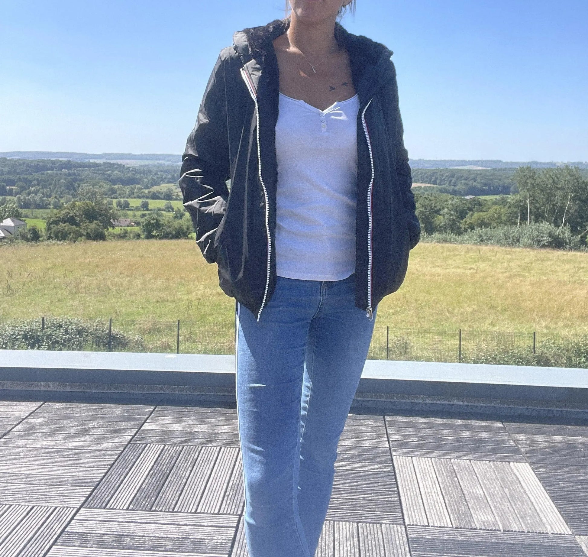 Woman wearing a black Laura Jo short waterproof jacket, white top, blue jeans outdoors