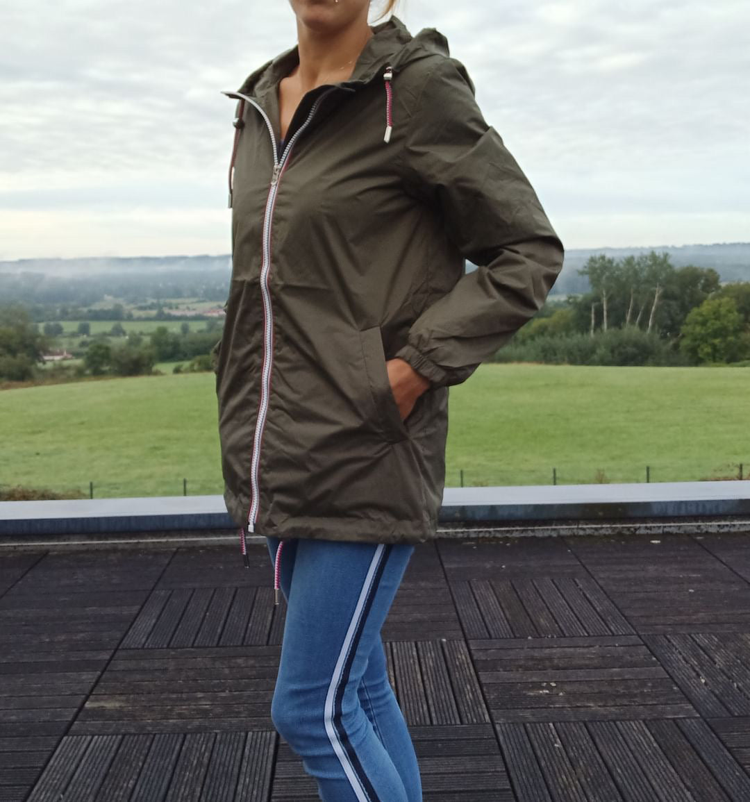 Woman wearing Laura Jo khaki raincoat from Le Petit Placard, jeans, outdoors with green field background.
