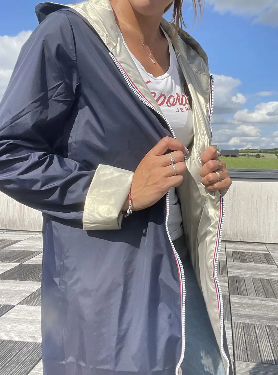 Manteau imperméable réversible long bleu marine et doré de Laura Jo, montré porté avec la capuche et la fermeture éclair visible.