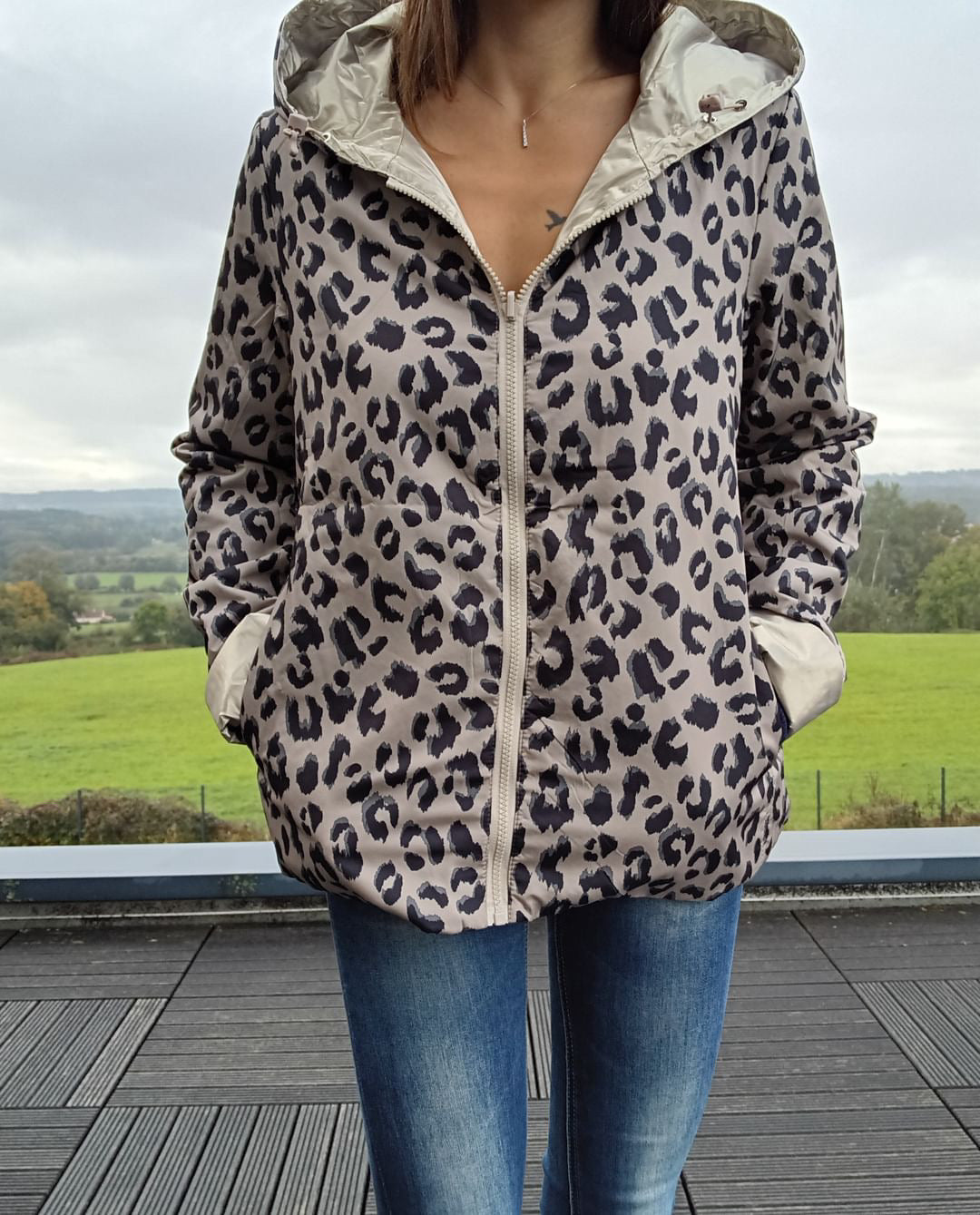 Veste réversible camargue courte à imprimé léopard beige et noir, capuche doublée, fermeture zippée centrale et poches, portée avec jeans.