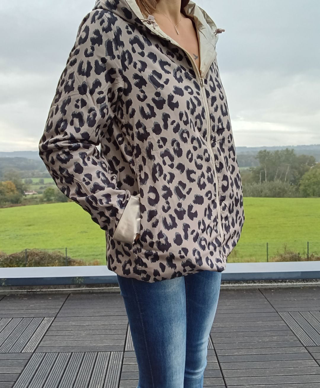 Veste légère réversible à motif léopard beige et noir, fermeture zip centrale, manches longues, poches, présentée en extérieur.