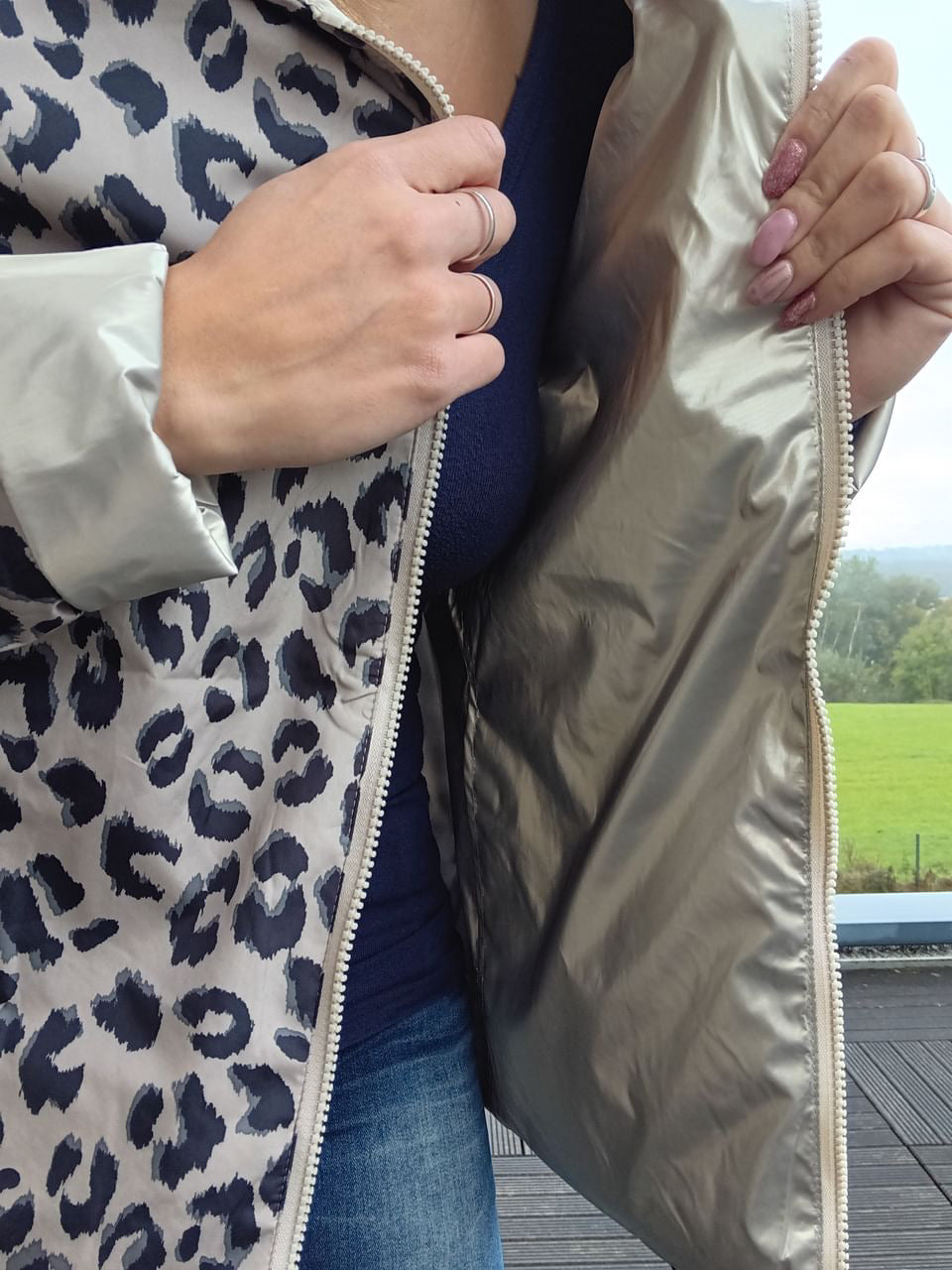Imperméable réversible court doré/léopard, fermeture éclair visible et garnissage léger; motif léopard côté intérieur, femme montrant le zip et le revers.
