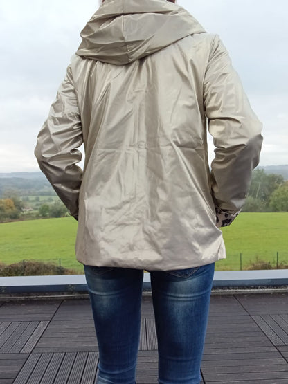 Imperméable réversible beige court vu de dos, capuche ample et garnissage léger, porté avec jeans sur une terrasse extérieure.