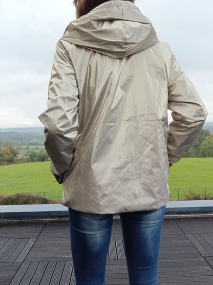 Imperméable réversible beige vu de dos, hoodée, longueur mi-hips, léger garnissage, porté sur jeans, paysage verdoyant en arrière-plan.