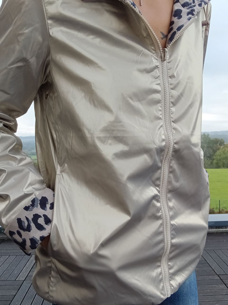 Imperméable court beige réversible avec capuche, zippé, doublure imitant léopard sur les bordures et les poignets, porté en jeans. vue de près 