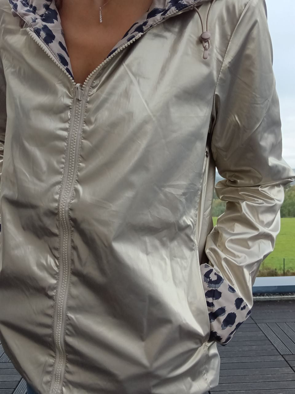 Imperméable reversibile mi-saison couleur beige clair, plié sur une fermeture éclair centrale, avec doublure patterned bleu et blanc et capuche décorative.
