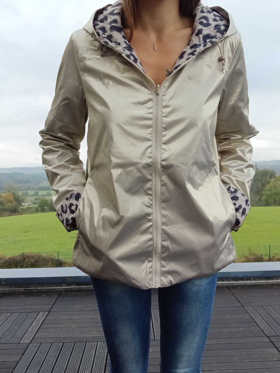 Imperméable réversible couleur beige clair avec capuche, doublure imprimé léopard sur l’intérieur et poignets, porté sur jeans.