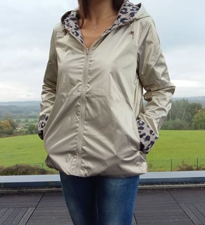 Imperméable réversible court couleur beige avec capuche; doublure à motif léopard visible aux revers et aux poignets, porté en extérieur avec jeans.