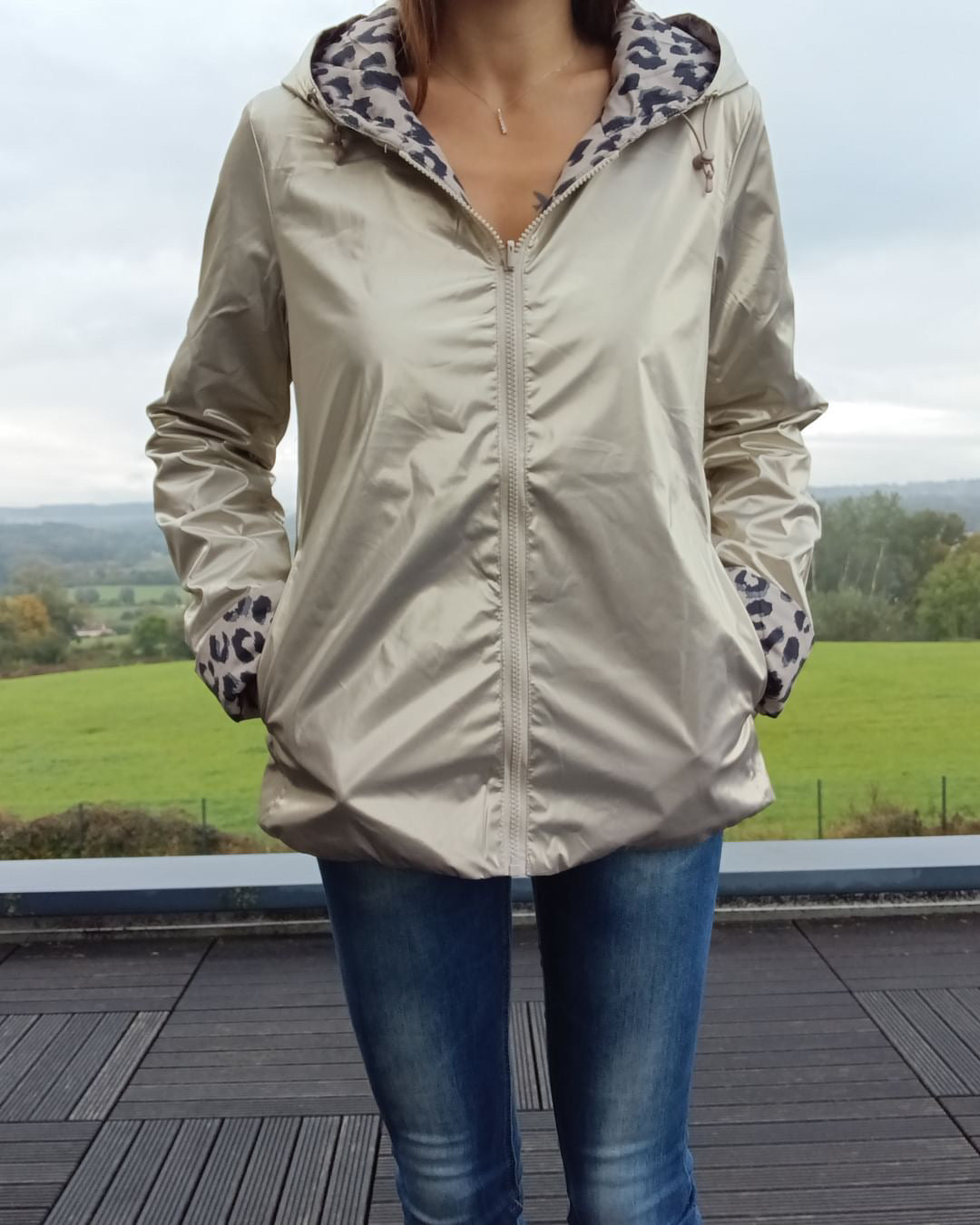 Imperméable réversible couleur beige avec doublure léopard à l’intérieur, fermeture zippée frontale et poches, porté en extérieur.