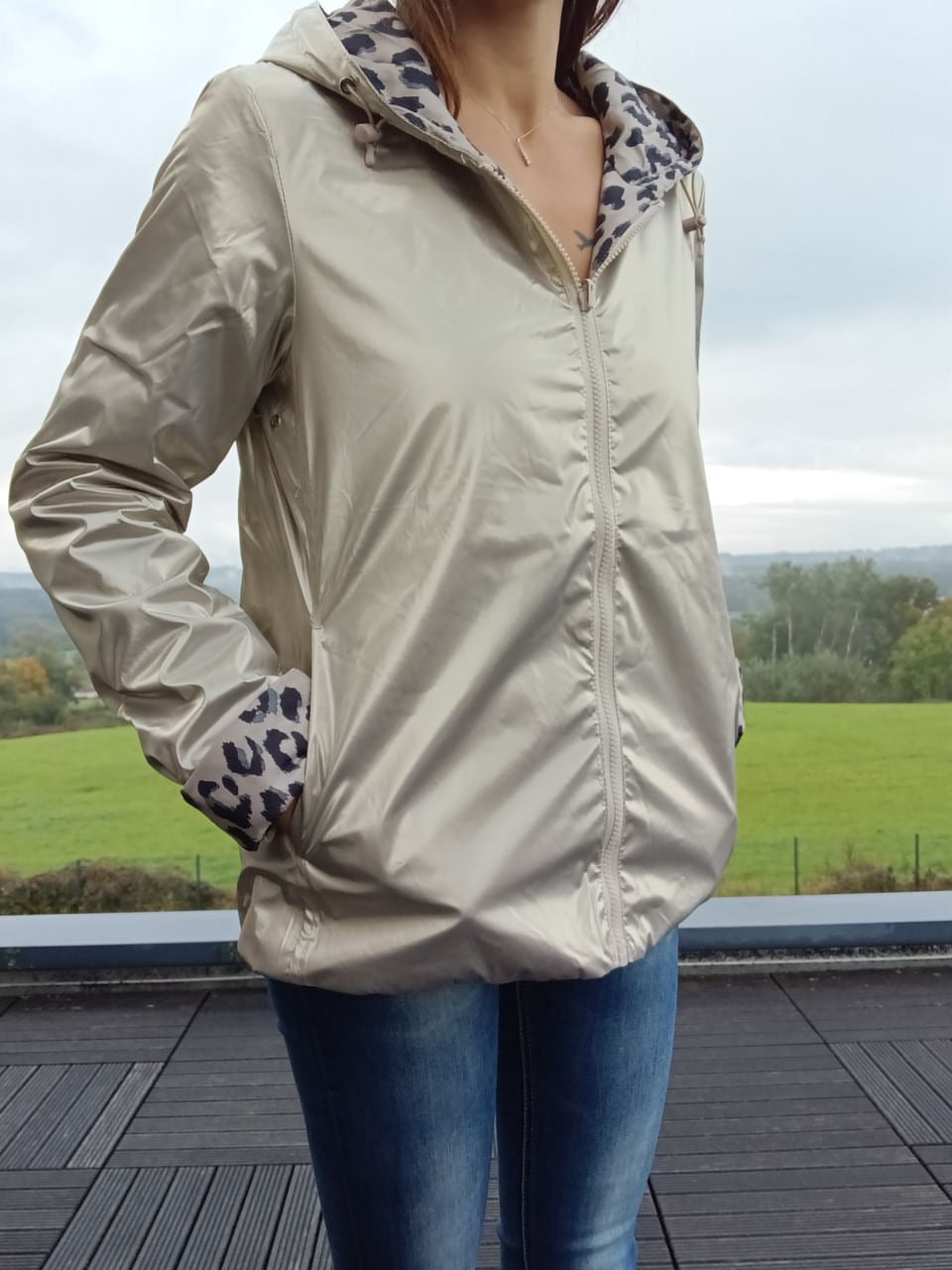 Imperméable réversible beige avec capuche, zippé devant, doublure à motif léopard sur l’intérieur et sur les manches; porté en extérieur.