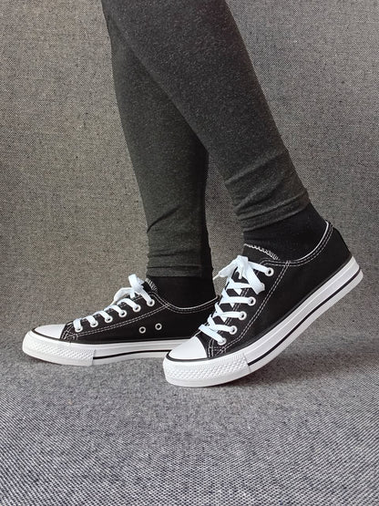Baskets basses noir et blanc femme style Converse bicolore, portées avec un legging gris