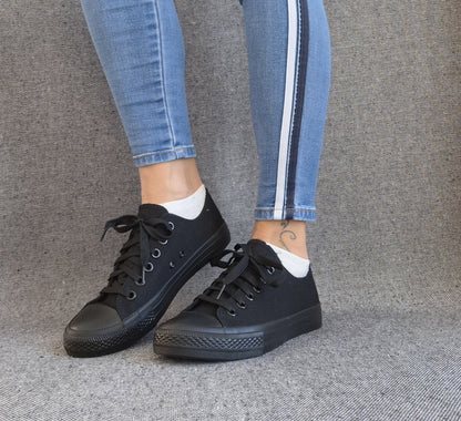 Baskets basses noir femme style Converse classique portées avec un jean slim à bandes latérales