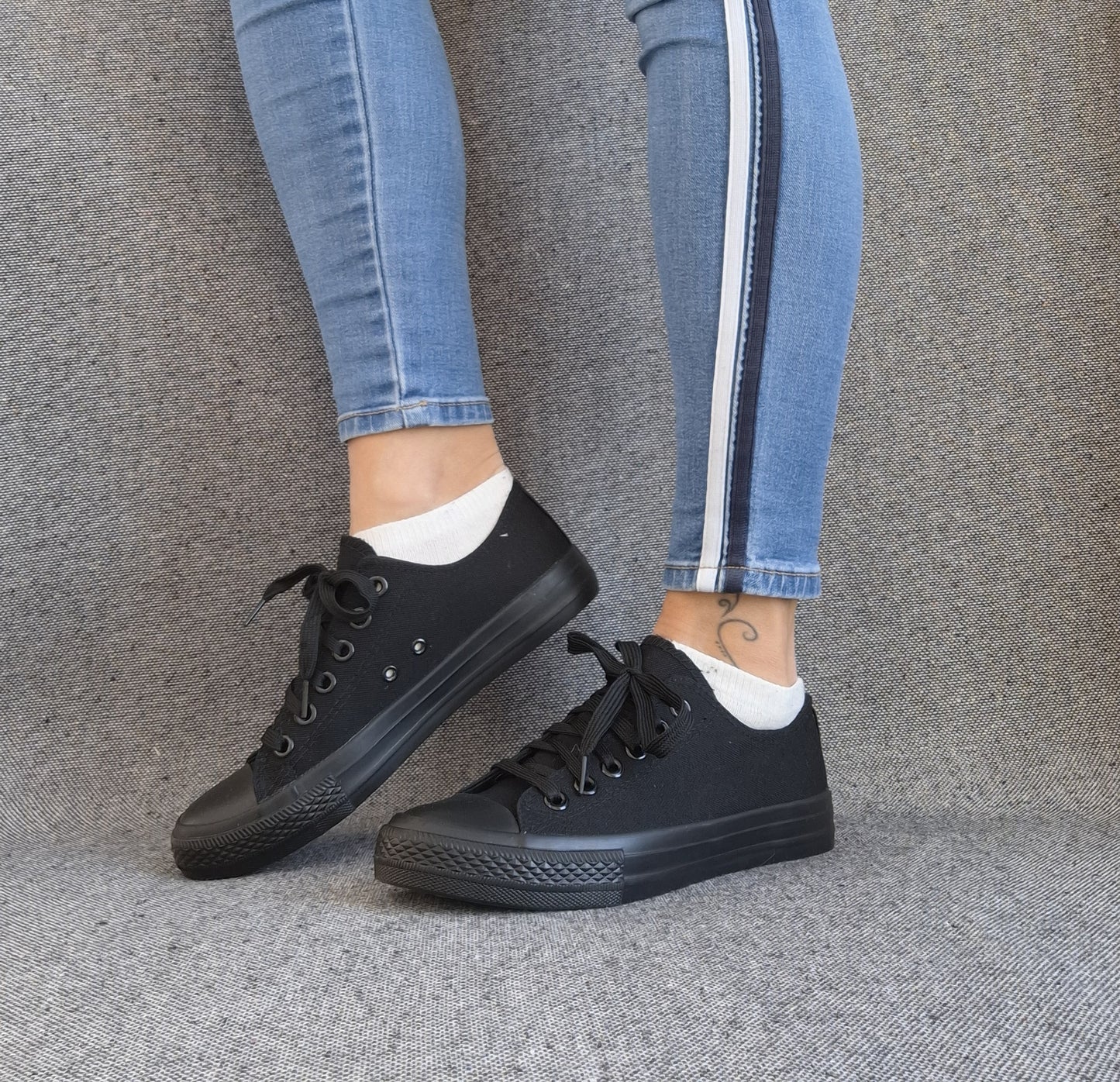 Baskets basses noir femme style Converse classique portées avec un jean skinny bleu à bandes latérales