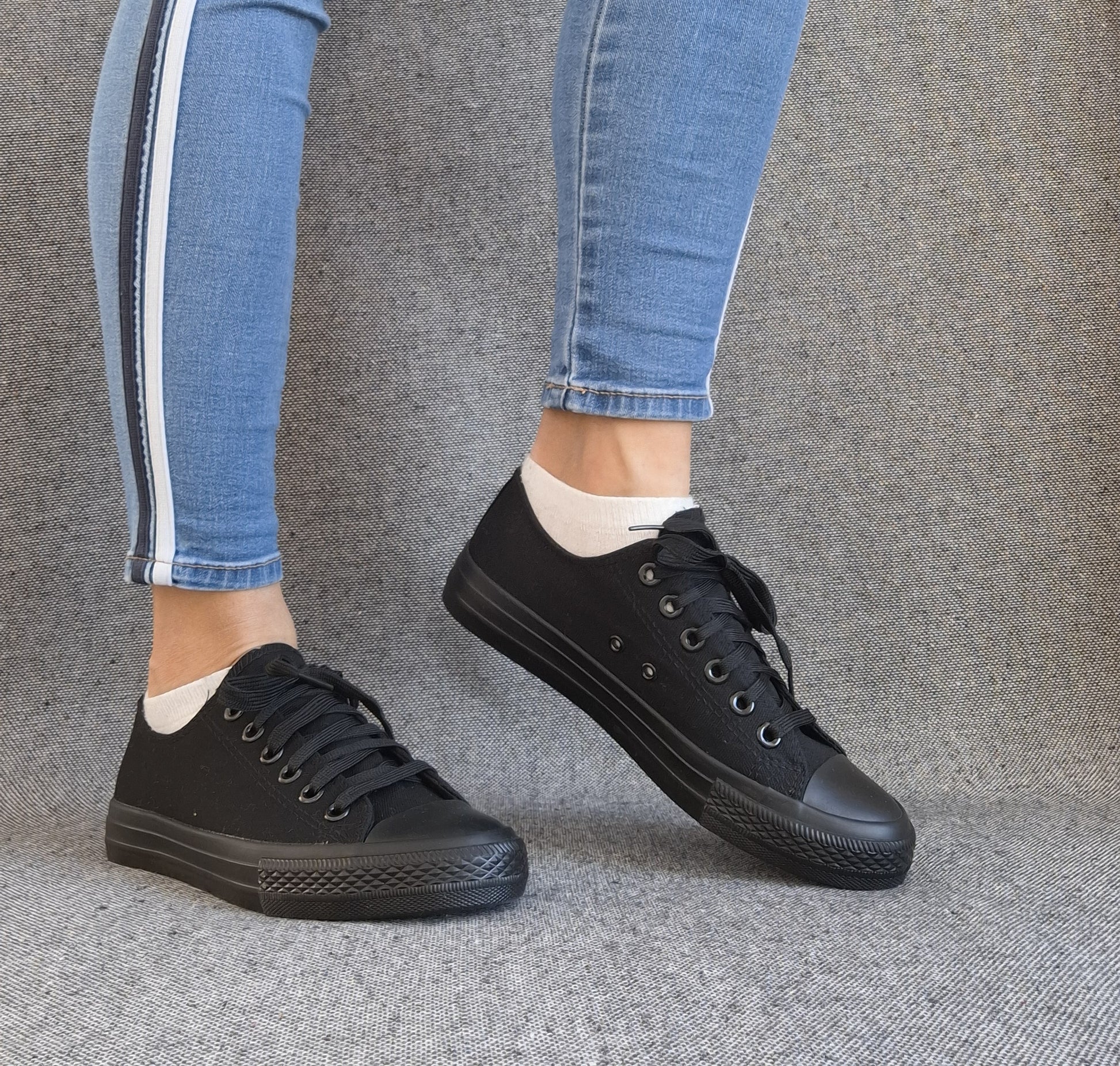 Baskets basses noir femme style Converse classique portées avec un jean slim bleu à bande blanche
