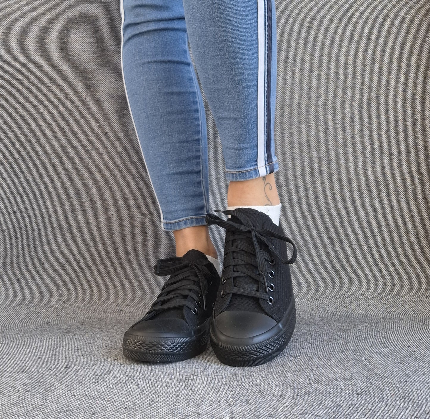 Baskets basses noir femme style Converse classique portées avec un jean slim bleu à bande latérale blanche