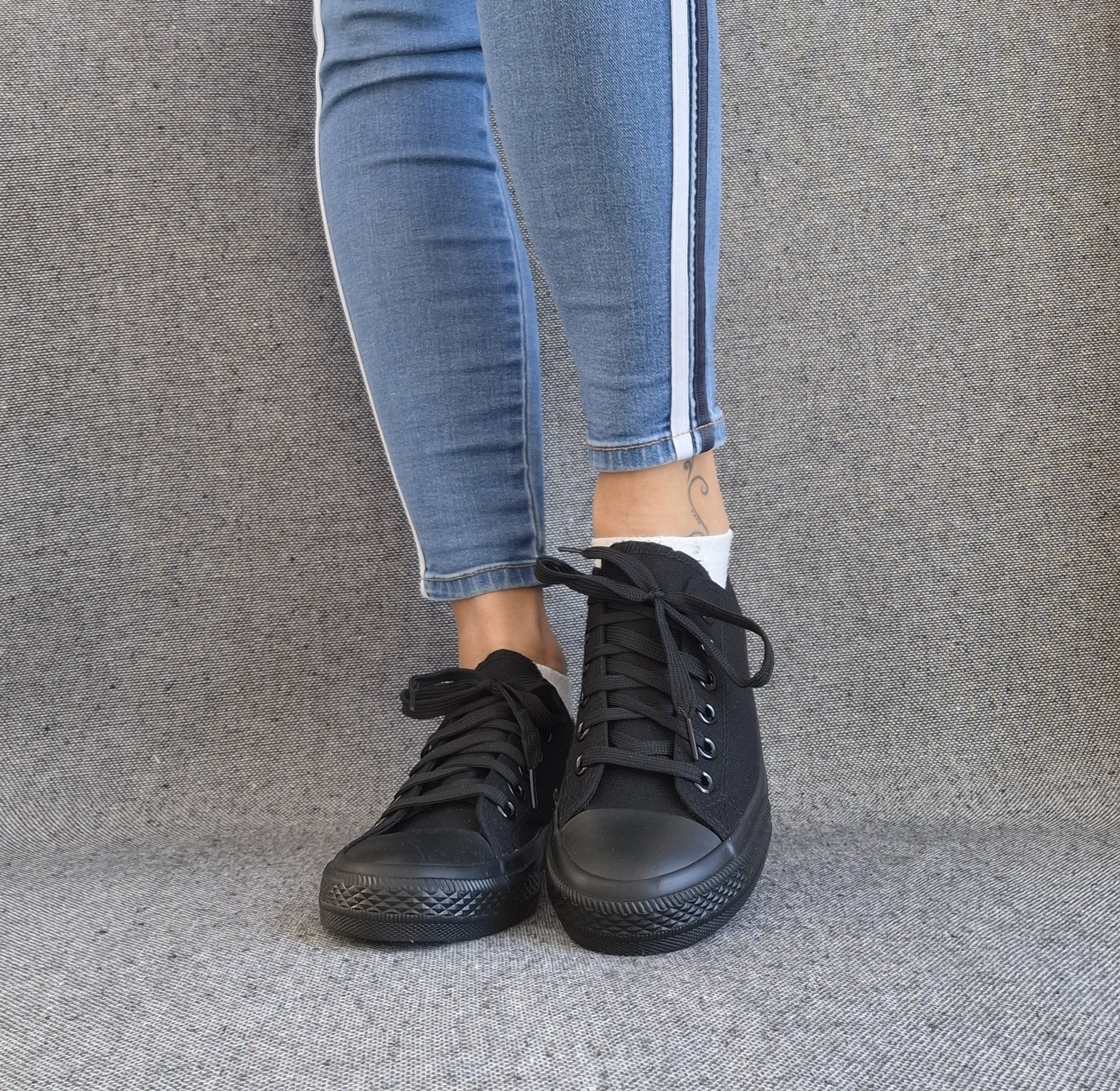 Baskets basses noir femme style Converse classique portées avec un jean slim bleu à bande latérale blanche