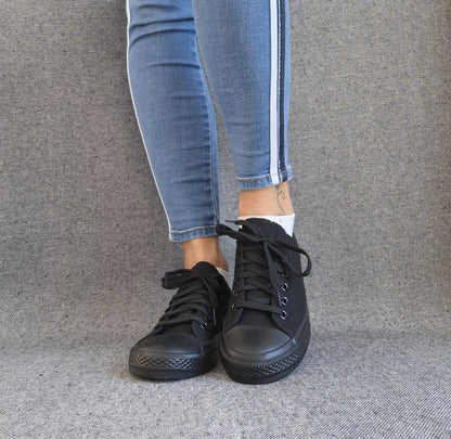 Baskets basses noir femme style Converse classique portées avec un jean slim bleu à bande latérale blanche