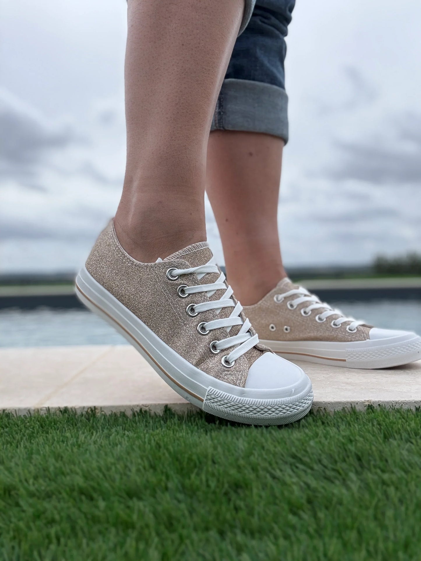 Baskets basses pailletées dorées femme style Converse à lacets blancs, portées sur gazon extérieur