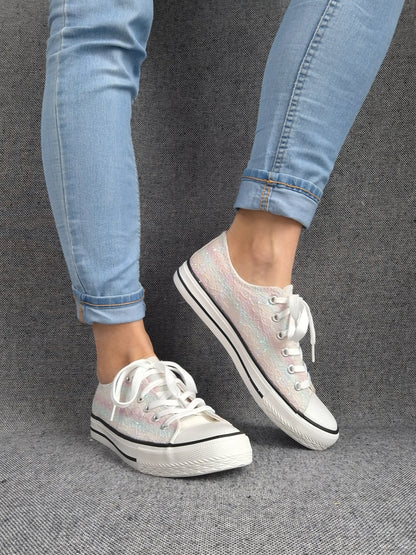 Chaussures baskets basses en tissu irisé multicolore avec lacets blancs, semelle blanche à rayures noires, portée avec jeans bleus.