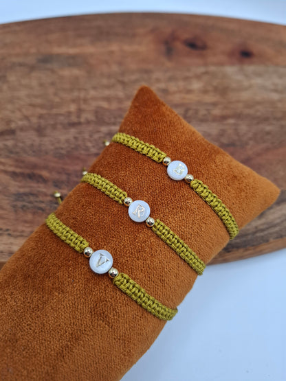 Three green braided bracelets with gold accent beads and lettered white charms on a brown cushion, Le Petit Placard style accessory.