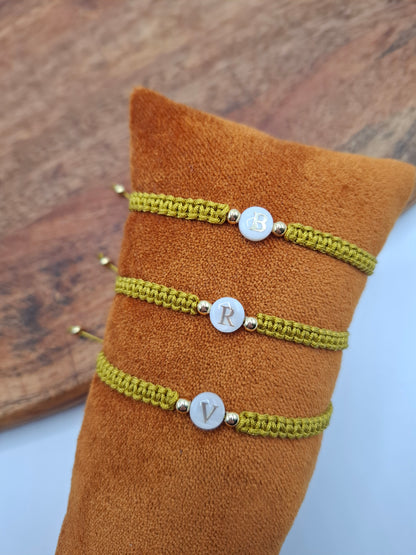 Three green woven initial bracelets with gold beads on brown velvet display, Le Petit Placard