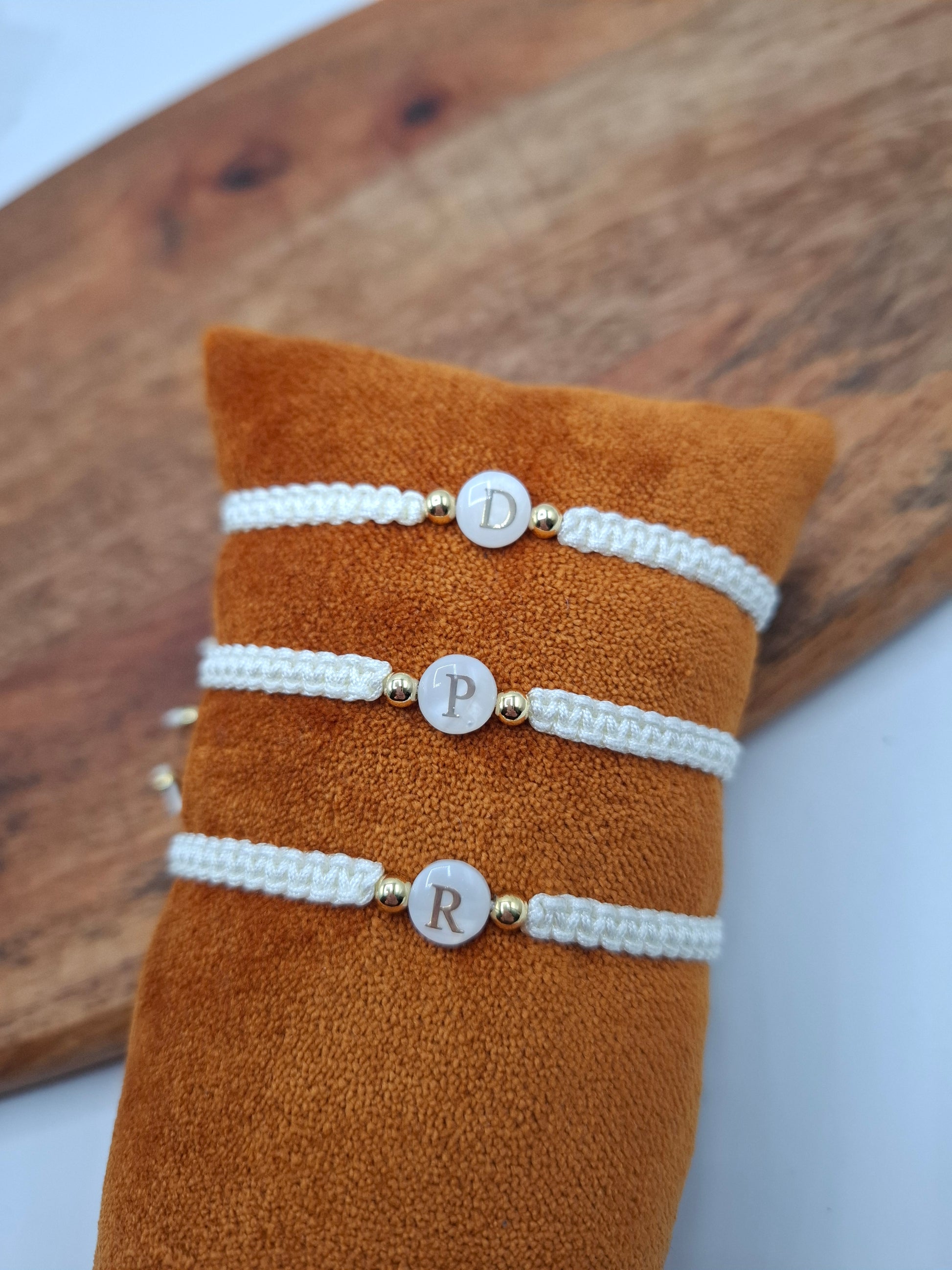 Personalized white braided bracelets with gold beads, displayed on orange fabric at Le Petit Placard
