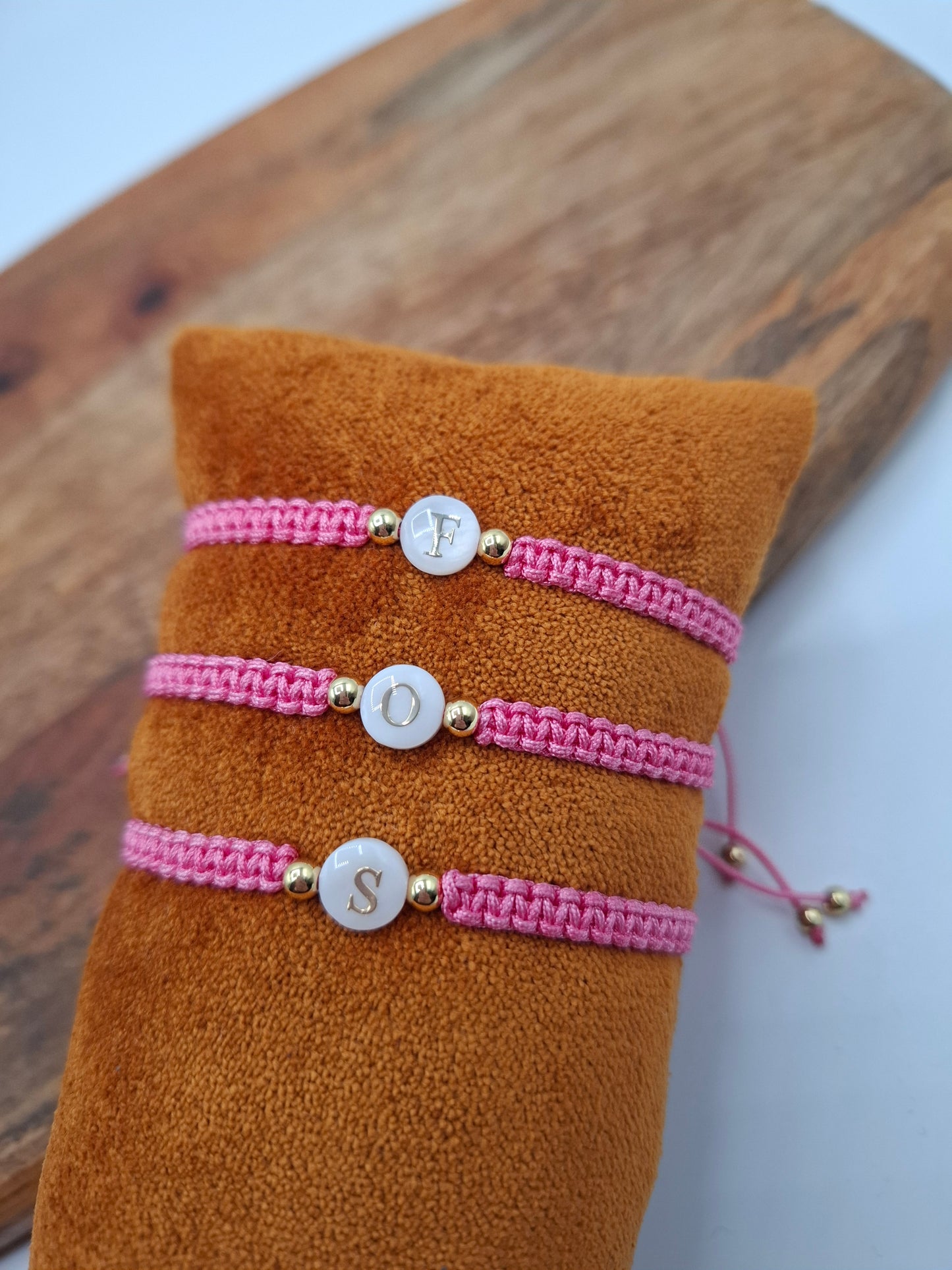 Pink woven initial bracelets with gold beads on a brown cushion, Le Petit Placard accessories