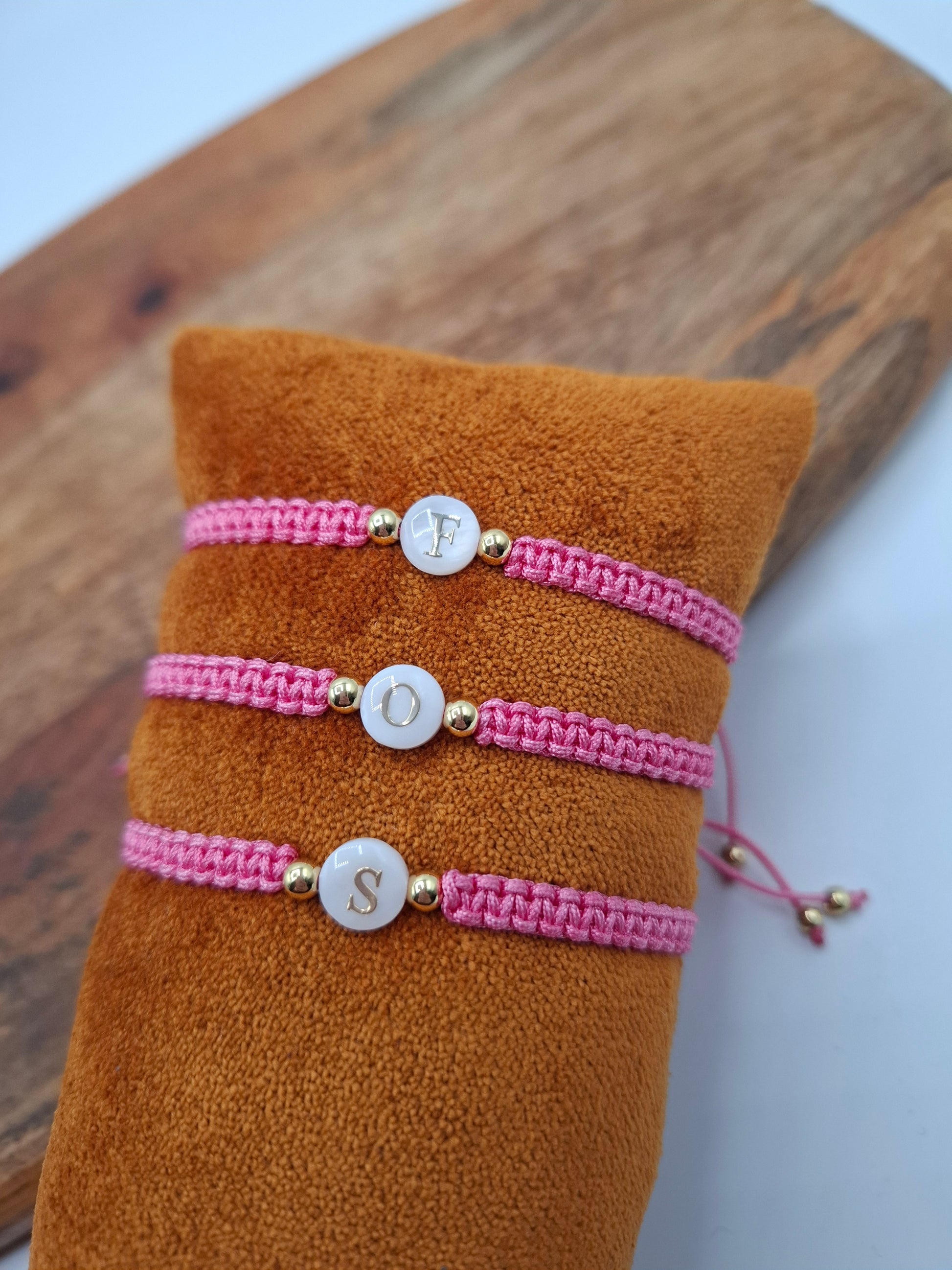 Pink woven initial bracelets with gold beads on a brown cushion, Le Petit Placard accessories