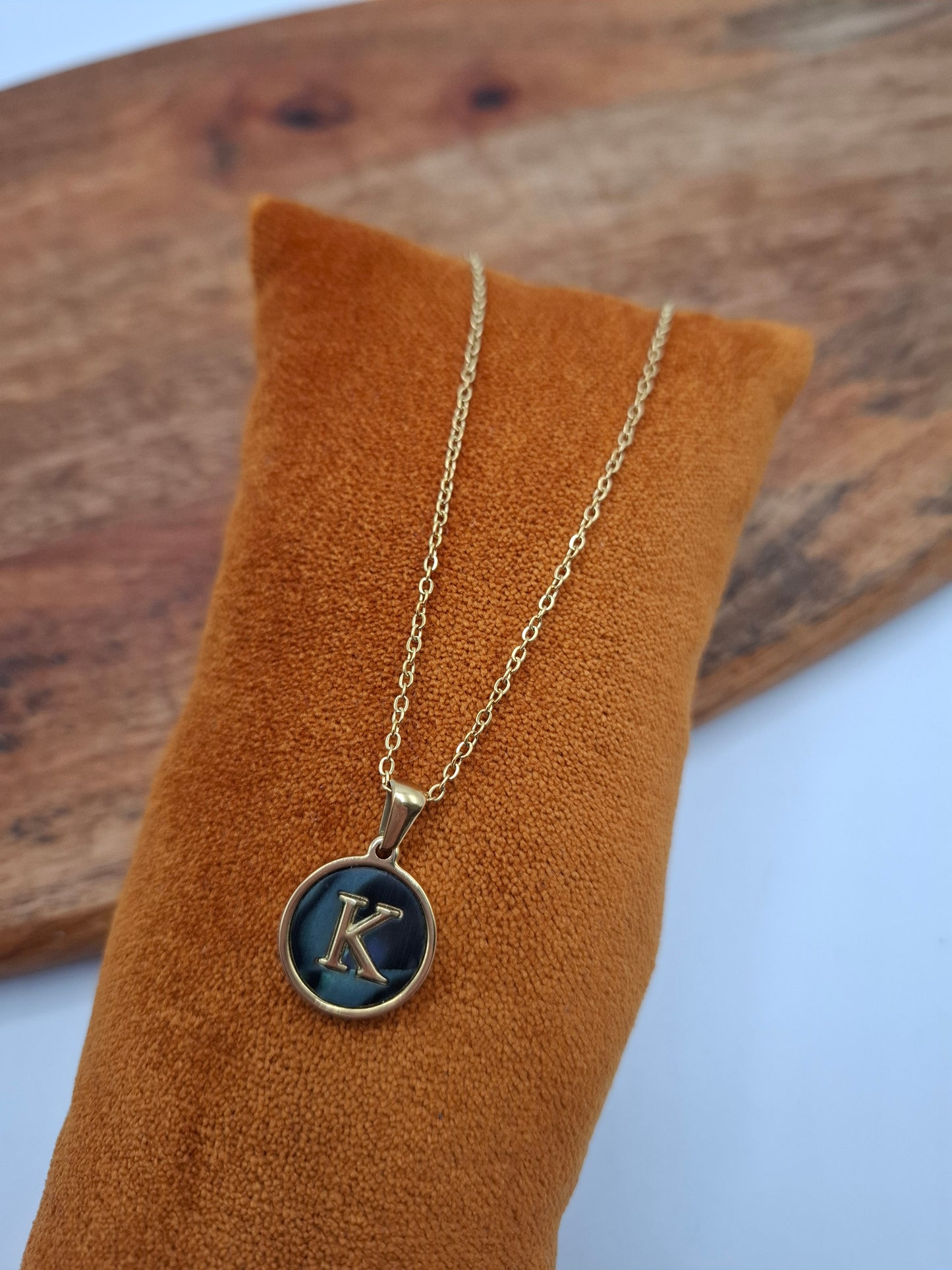 Gold letter K pendant necklace on mustard suede cushion, Le Petit Placard accessory