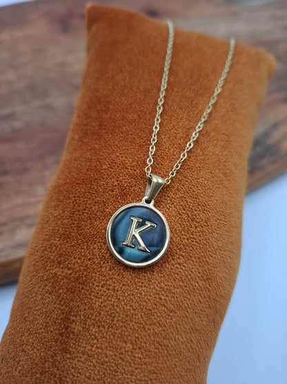 Gold initial K pendant necklace on a blue enamel disc, displayed on brown velvet.