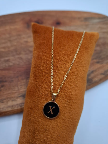 Gold letter X pendant necklace on black background, displayed on brown velvet cushion, Le Petit Placard