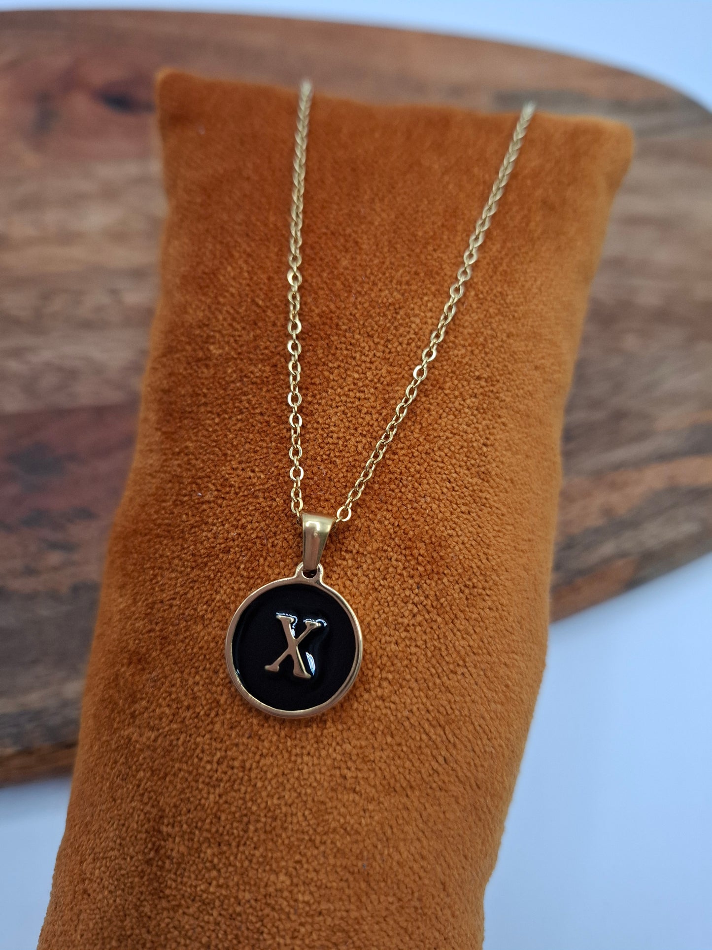 Gold initial X necklace pendant on black enamel, displayed on brown velvet at Le Petit Placard