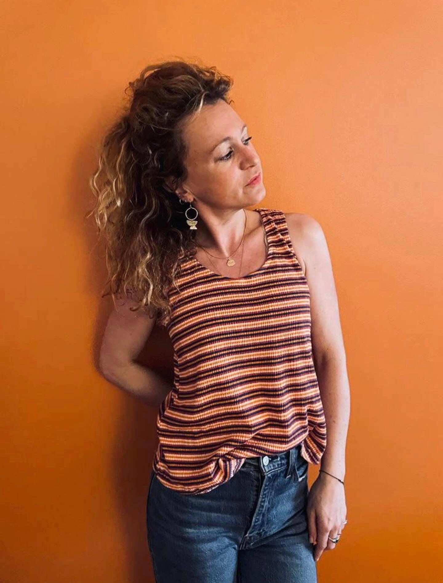Femme portant un débardeur à rayures brun et jaune upcyclé en coton lin, associé à un jean, fond orange