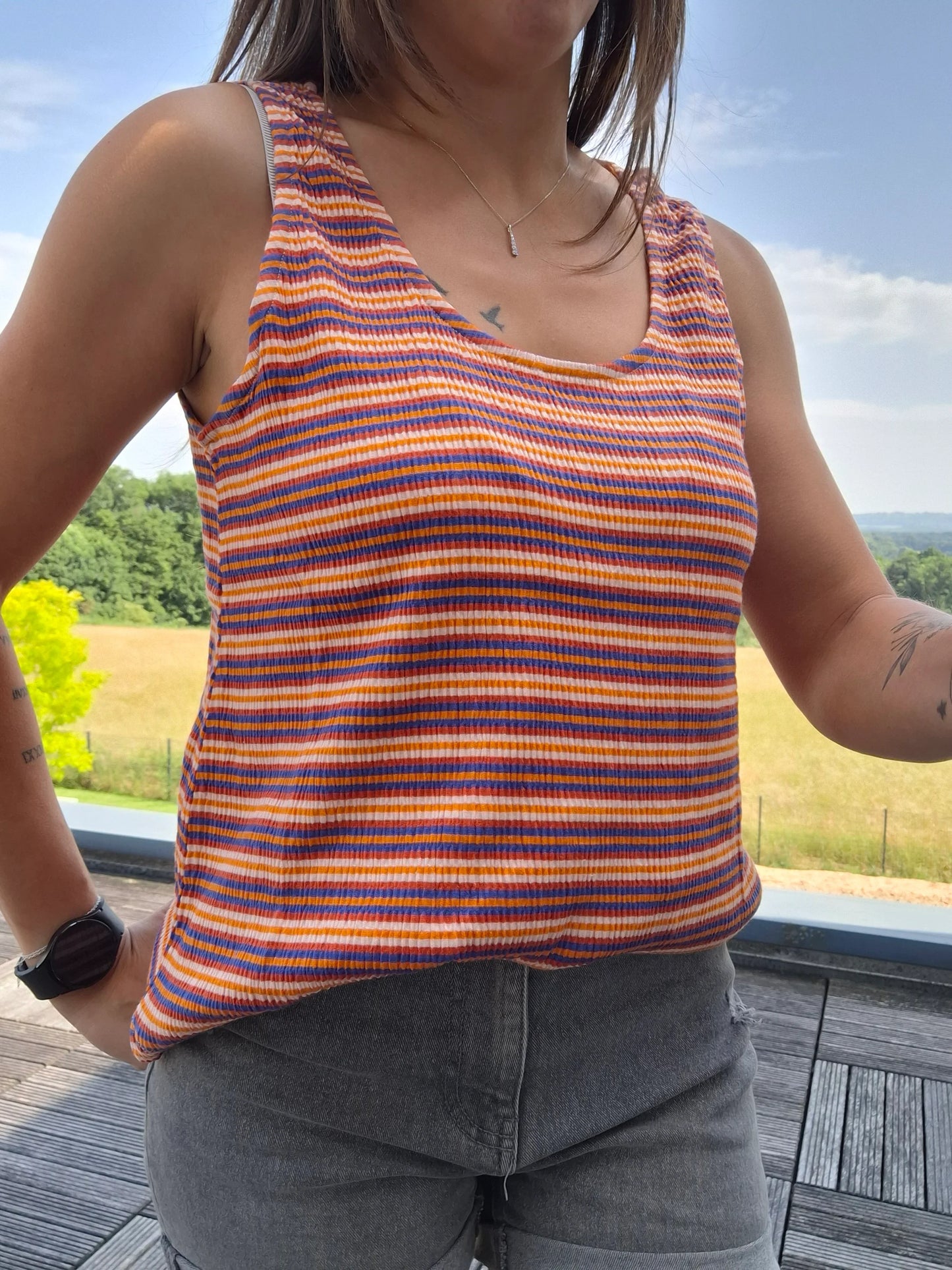 Débardeur upcyclé à rayures orange, bleu et blanc en coton/lin porté avec un jean gris, en extérieur