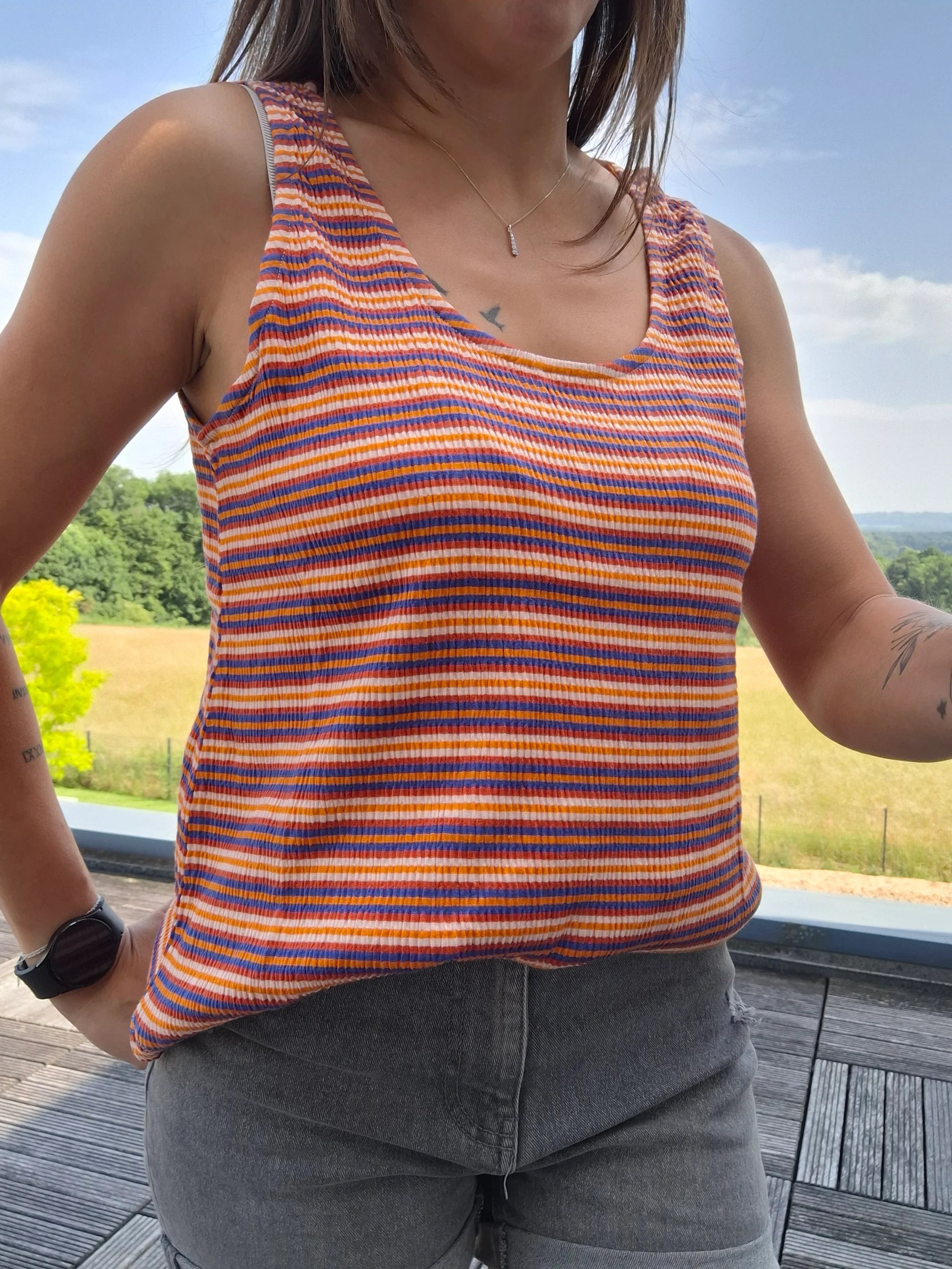 Débardeur upcyclé à rayures orange, bleu et blanc en coton/lin porté avec un jean gris, en extérieur