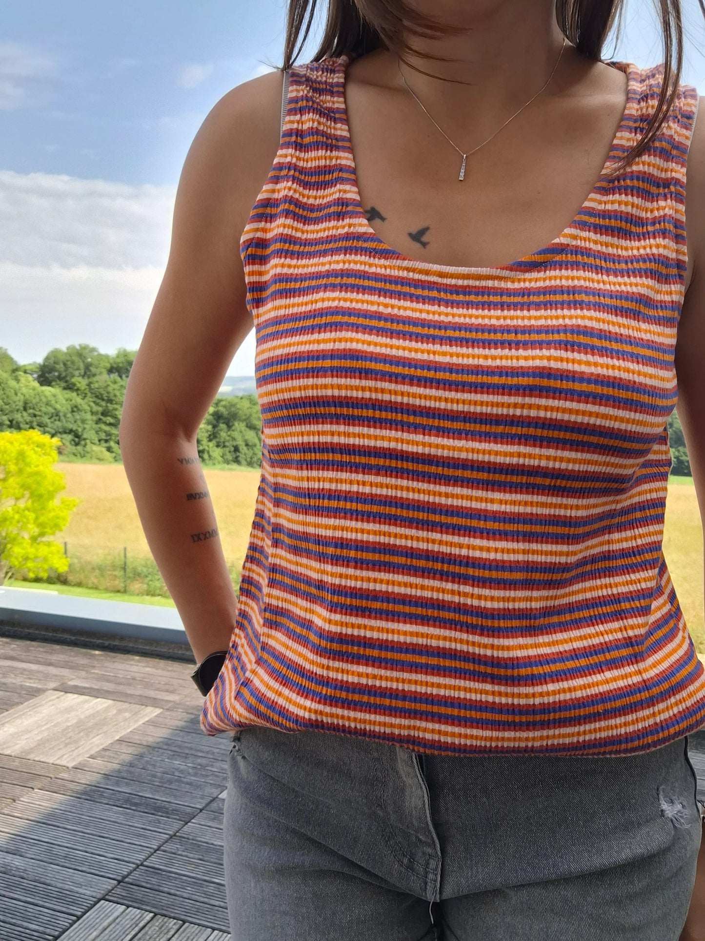 Débardeur à rayures upcyclé en coton/lin orange, bleu et blanc porté par une femme en extérieur
