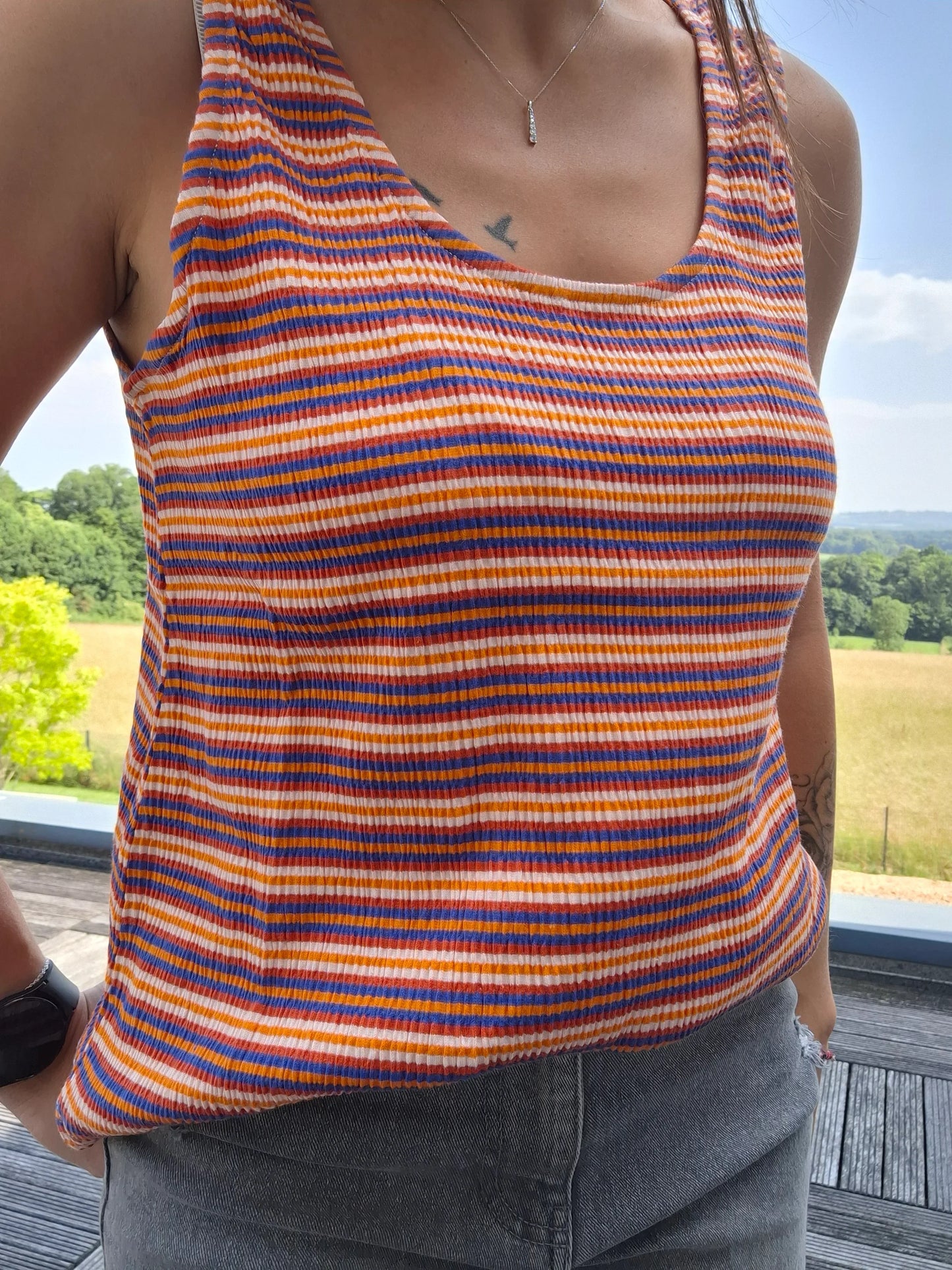 Débardeur à rayures upcyclé en coton/lin porté par une femme, rayures orange, rouge et bleu, fond nature ensoleillé