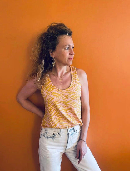 Femme portant un débardeur bariolé jaune upcyclé coton/lin à imprimé zèbre rose et or, jean blanc, fond orange