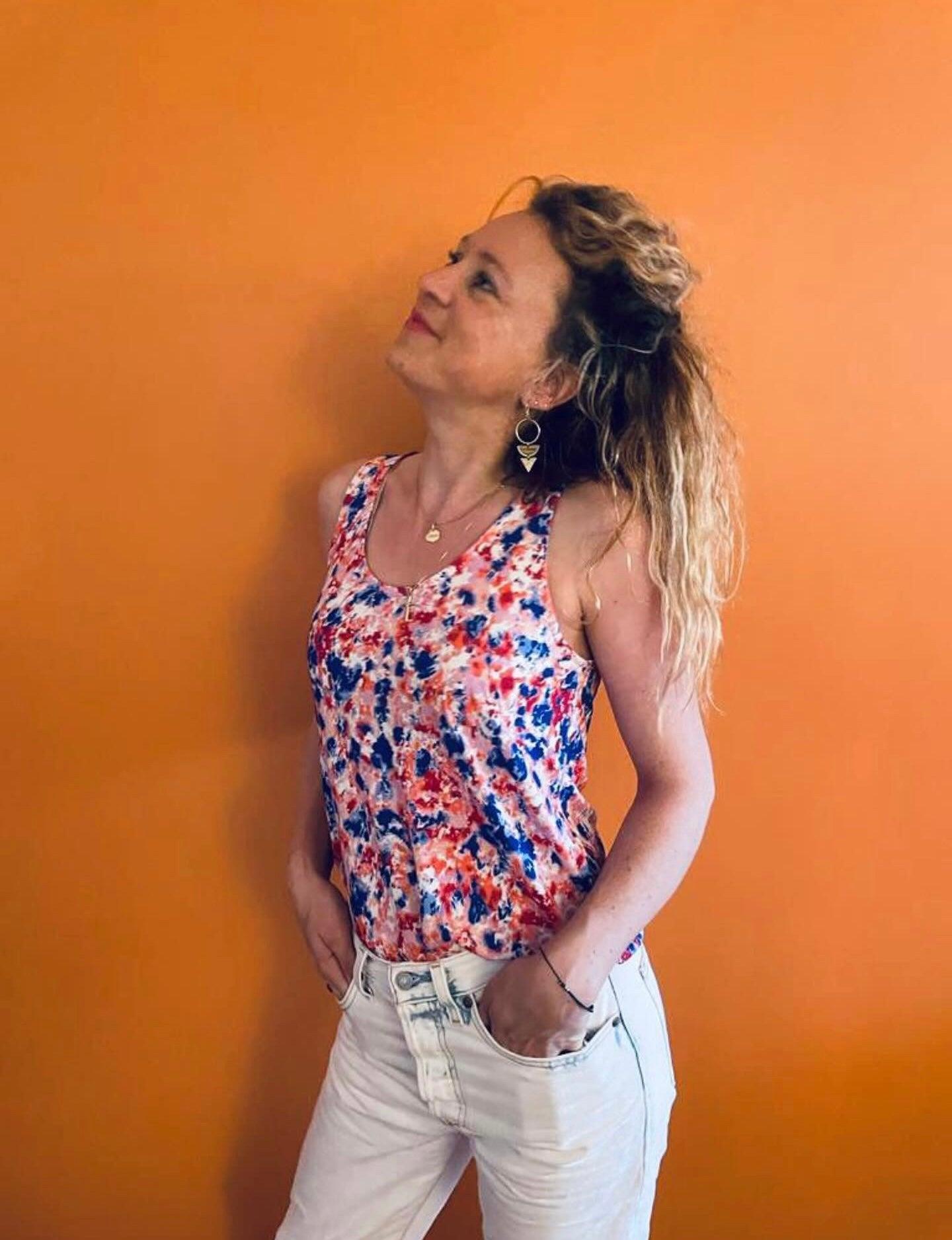Femme portant un débardeur fleuri bleu et rouge upcyclé en coton/lin, associé à un jean blanc, fond orange