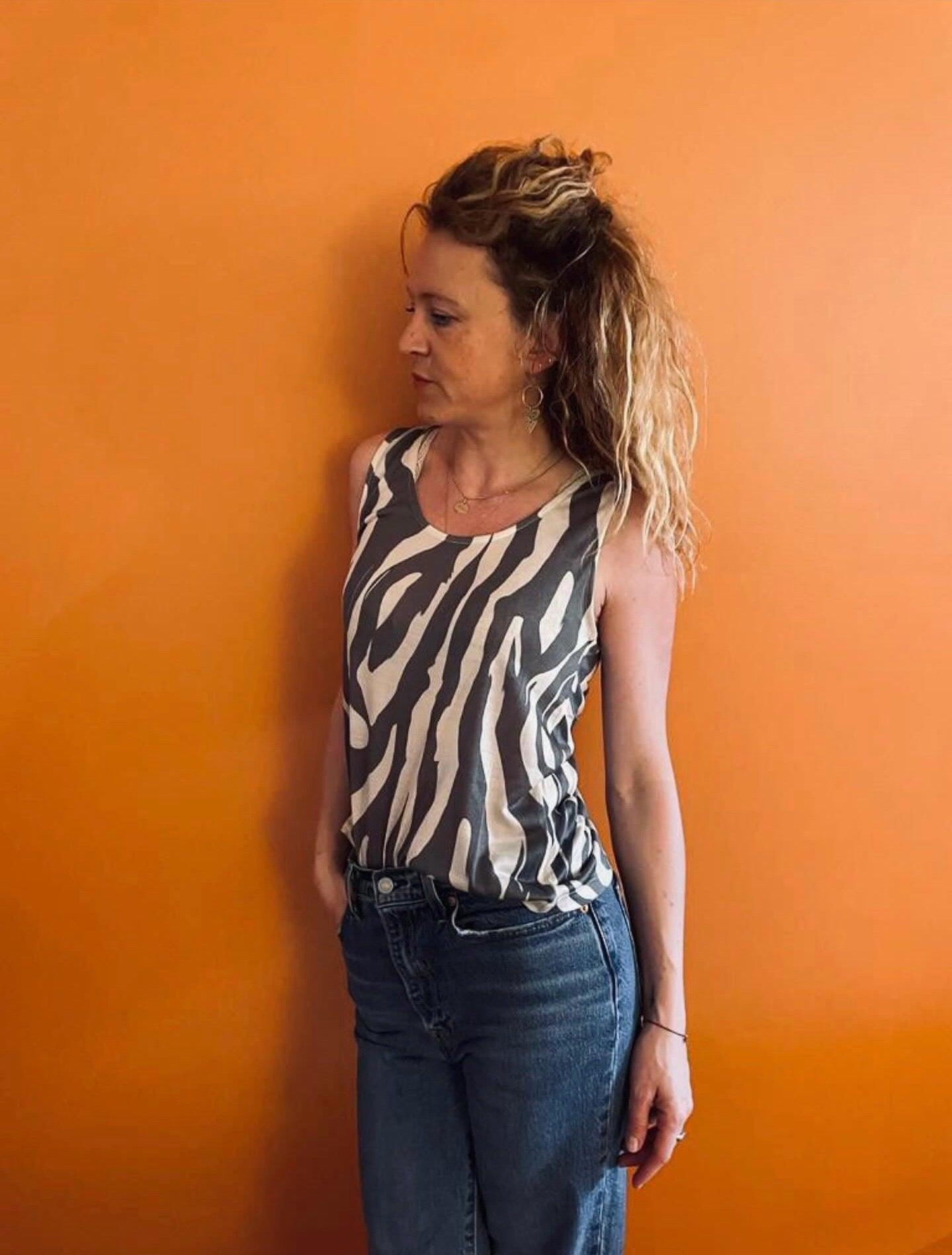 Femme portant un débardeur motif zèbre upcyclé en coton/lin noir et blanc, associé à un jean, fond orange