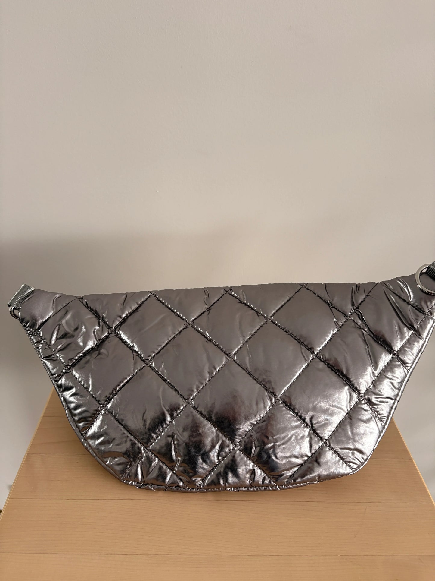 Sac banane XL matelassé effet doudoune argenté métallisé, grand format, posé sur une surface en bois